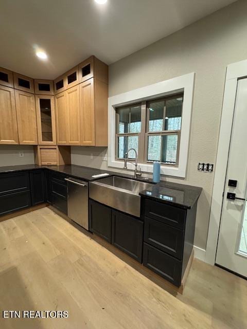 kitchen with dishwasher, dark countertops, light wood-style flooring, glass insert cabinets, and a sink