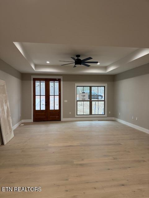 empty room with light wood finished floors, baseboards, a raised ceiling, and french doors