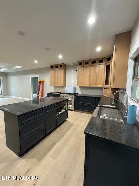 kitchen featuring recessed lighting, stainless steel range with gas stovetop, a sink, light wood-type flooring, and dark stone counters