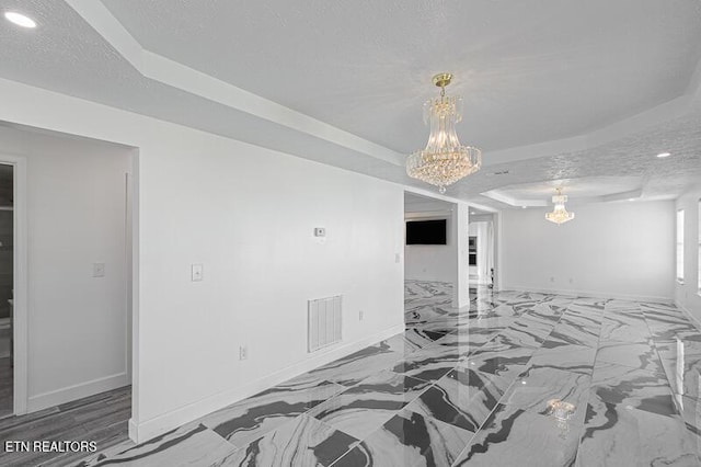 unfurnished room featuring a textured ceiling, a tray ceiling, and an inviting chandelier