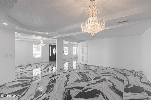 interior space featuring a textured ceiling, an inviting chandelier, and a raised ceiling