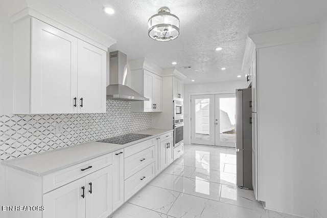 kitchen featuring french doors, a textured ceiling, stainless steel appliances, wall chimney range hood, and white cabinetry