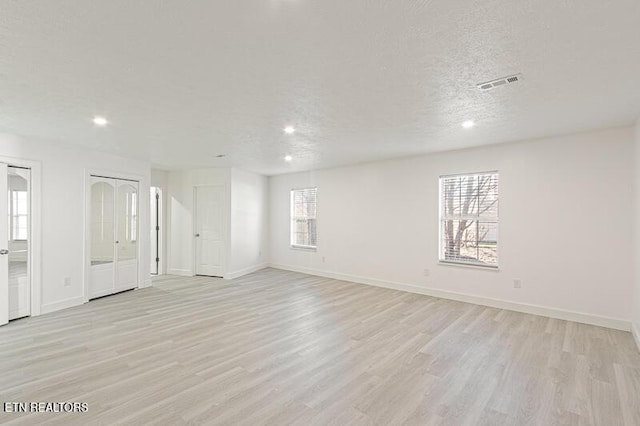 unfurnished living room with light hardwood / wood-style floors, a textured ceiling, and a wealth of natural light