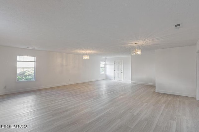 spare room featuring a wealth of natural light, a notable chandelier, and light wood-type flooring