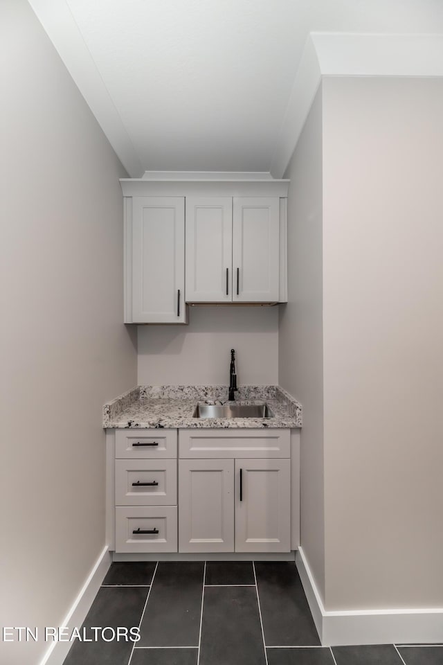 bar with sink, white cabinetry, and light stone counters