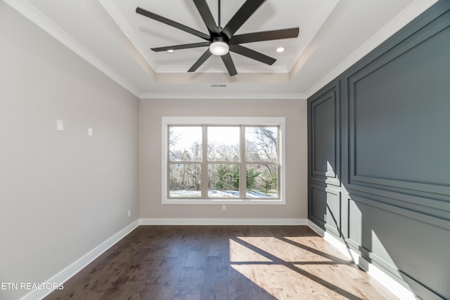 unfurnished room with ceiling fan, a tray ceiling, dark hardwood / wood-style floors, and ornamental molding