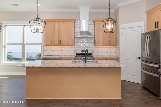 kitchen featuring pendant lighting, stainless steel fridge with ice dispenser, wall chimney range hood, light brown cabinetry, and an island with sink