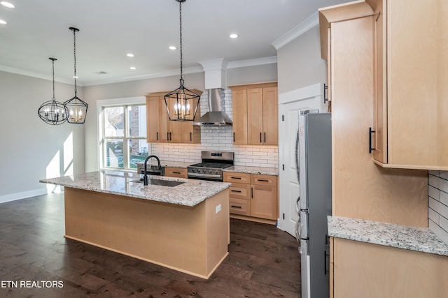 kitchen featuring a center island with sink, sink, appliances with stainless steel finishes, wall chimney range hood, and light brown cabinets