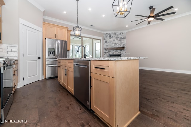 kitchen with an island with sink, hanging light fixtures, ornamental molding, appliances with stainless steel finishes, and light brown cabinets