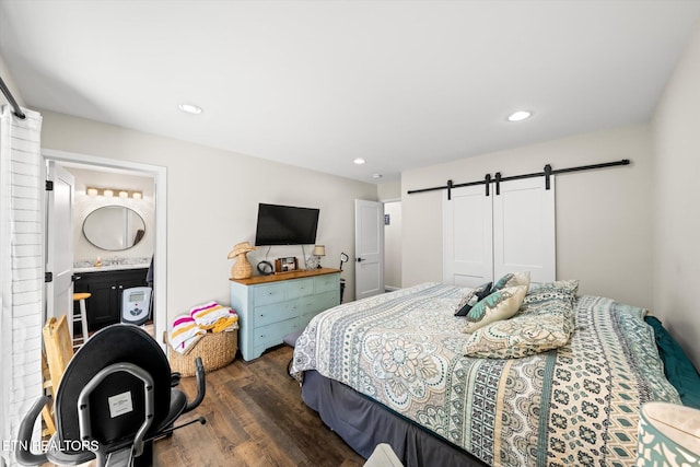 bedroom featuring connected bathroom, dark hardwood / wood-style flooring, and a barn door