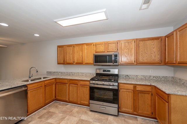 kitchen with light stone countertops, kitchen peninsula, sink, and stainless steel appliances