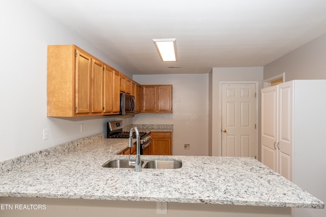 kitchen featuring kitchen peninsula, stainless steel appliances, sink, and light stone counters