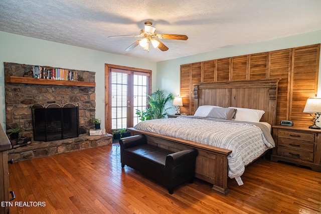 bedroom featuring wood walls, ceiling fan, a textured ceiling, hardwood / wood-style floors, and a fireplace