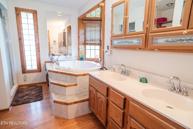 bathroom featuring vanity, tiled bath, wood-type flooring, and plenty of natural light