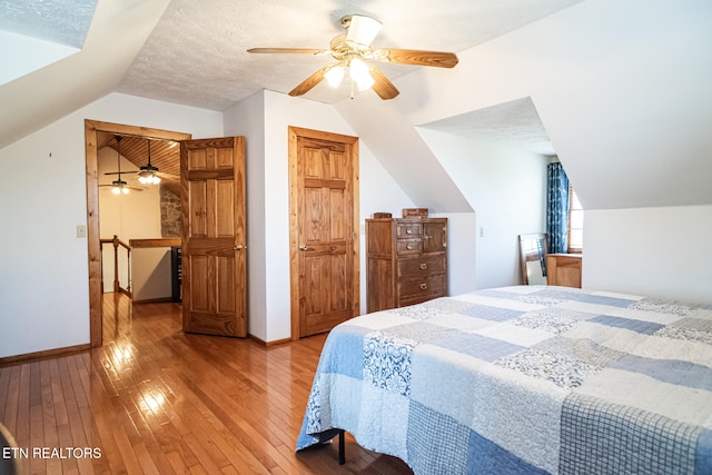 bedroom with a textured ceiling, hardwood / wood-style floors, ceiling fan, and vaulted ceiling