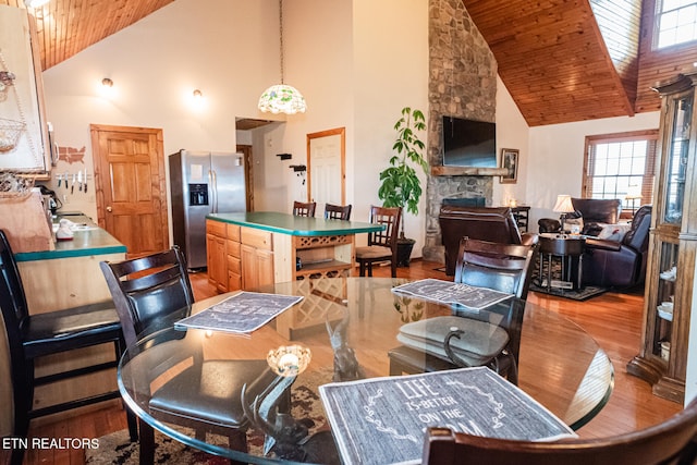 dining room featuring high vaulted ceiling, light wood-type flooring, wood ceiling, and a fireplace