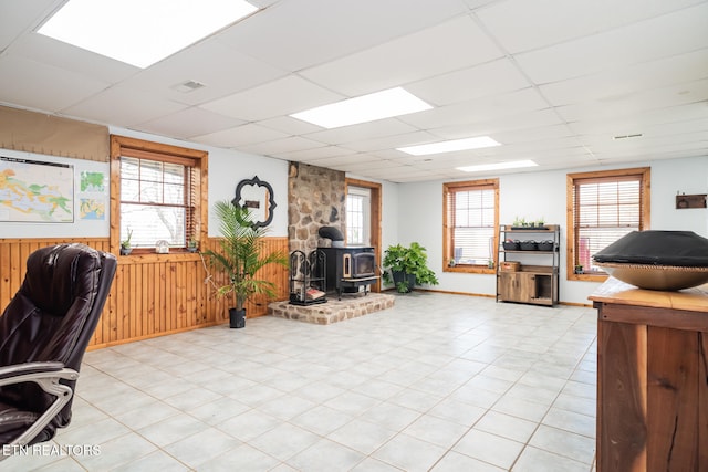 tiled office space with plenty of natural light, wooden walls, a wood stove, and a drop ceiling