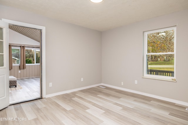 spare room featuring vaulted ceiling, plenty of natural light, a textured ceiling, and light wood-type flooring