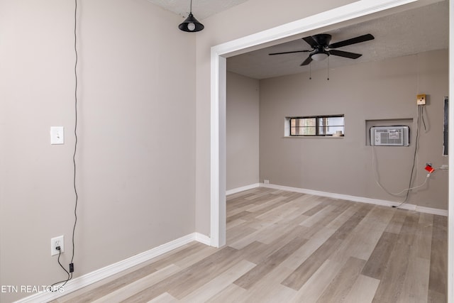 interior space with a wall mounted air conditioner, a textured ceiling, light wood-type flooring, and ceiling fan