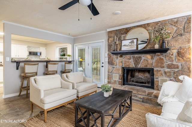 living room featuring crown molding, ceiling fan, light tile patterned floors, a fireplace, and a textured ceiling