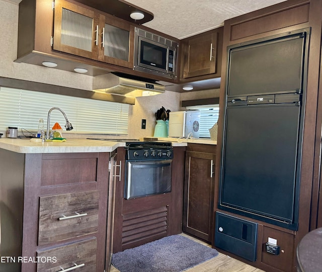 kitchen featuring extractor fan, stainless steel microwave, light hardwood / wood-style flooring, and dark brown cabinetry