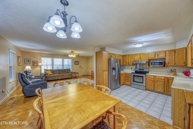 kitchen with ceiling fan with notable chandelier, hanging light fixtures, a textured ceiling, light tile patterned flooring, and appliances with stainless steel finishes