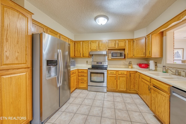 kitchen featuring appliances with stainless steel finishes, sink, light tile patterned floors, and a textured ceiling