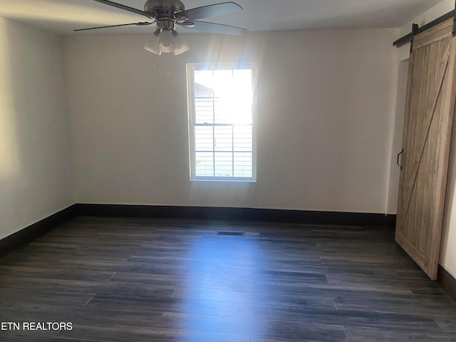 spare room with ceiling fan, a barn door, and dark hardwood / wood-style floors