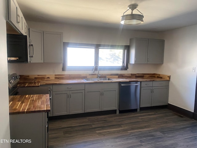 kitchen featuring sink, wooden counters, stainless steel dishwasher, gray cabinets, and dark hardwood / wood-style flooring