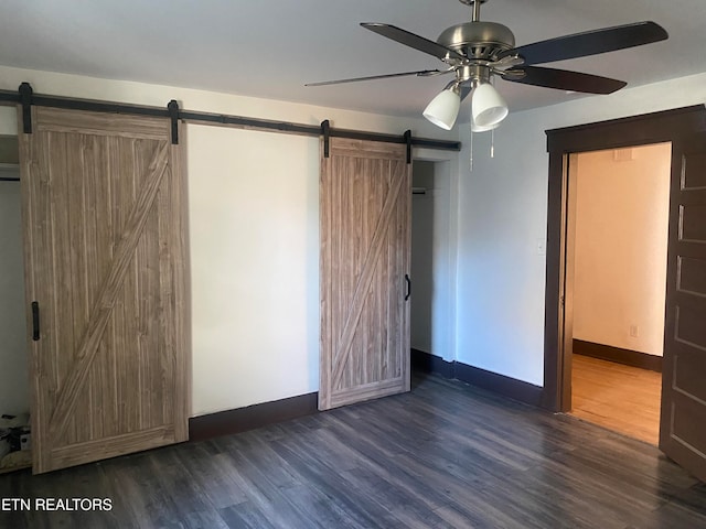 unfurnished bedroom with dark wood-type flooring, a barn door, and ceiling fan