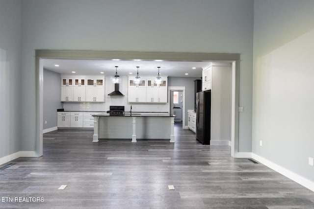 kitchen with stainless steel refrigerator, dark hardwood / wood-style floors, hanging light fixtures, a kitchen island with sink, and white cabinets