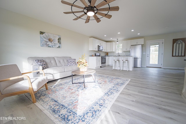 living room featuring ceiling fan, sink, and light hardwood / wood-style flooring