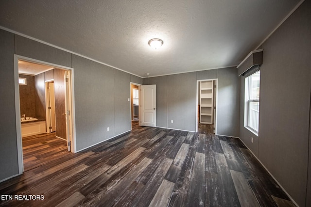 unfurnished bedroom with a closet, a spacious closet, connected bathroom, a textured ceiling, and dark wood-type flooring