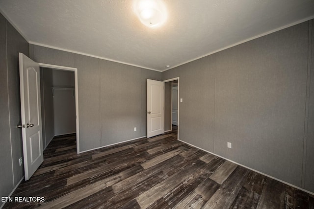 unfurnished bedroom featuring a spacious closet, dark hardwood / wood-style flooring, crown molding, and a closet