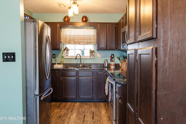 kitchen featuring sink, stainless steel appliances, dark hardwood / wood-style floors, dark stone countertops, and a textured ceiling