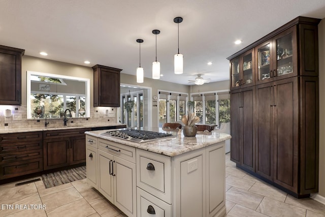 kitchen with ceiling fan, a center island, decorative backsplash, sink, and stainless steel gas cooktop