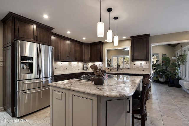 kitchen with a kitchen island, hanging light fixtures, light stone countertops, stainless steel appliances, and dark brown cabinets