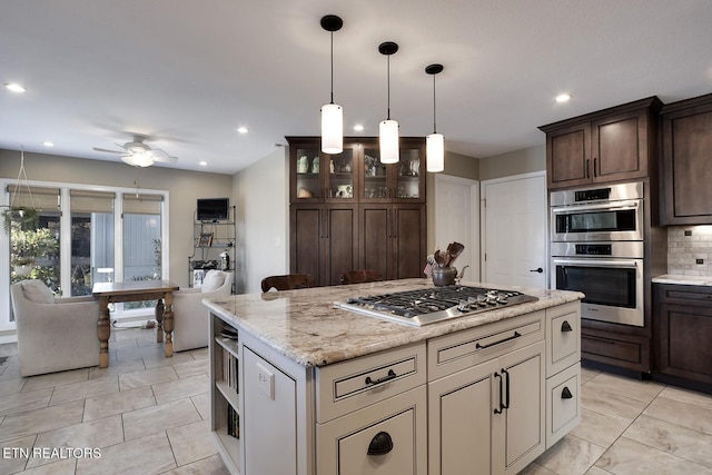 kitchen featuring ceiling fan, stainless steel appliances, decorative backsplash, dark brown cabinetry, and a center island