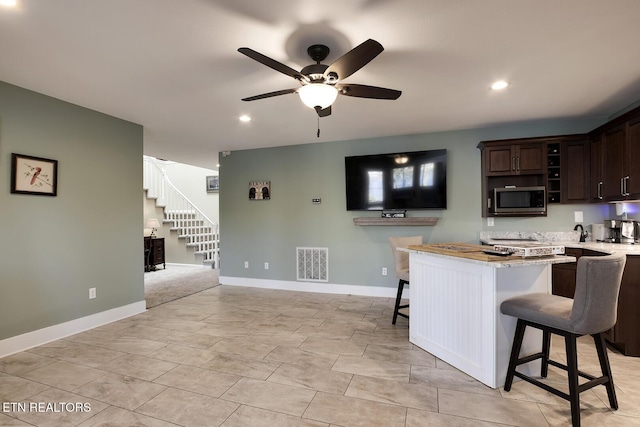 kitchen featuring light stone countertops, a breakfast bar area, dark brown cabinetry, and ceiling fan