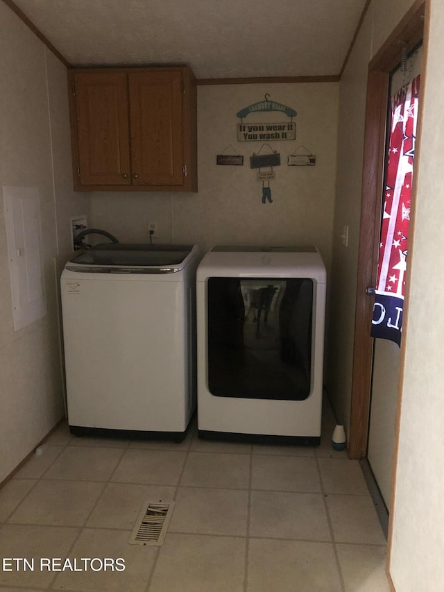 clothes washing area featuring cabinets, washing machine and dryer, and light tile patterned floors