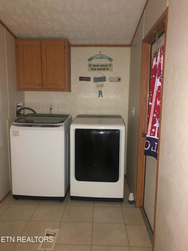 laundry room featuring ornamental molding, a textured ceiling, light tile patterned floors, cabinets, and washing machine and clothes dryer