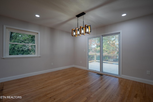 spare room featuring plenty of natural light, light hardwood / wood-style floors, and a chandelier