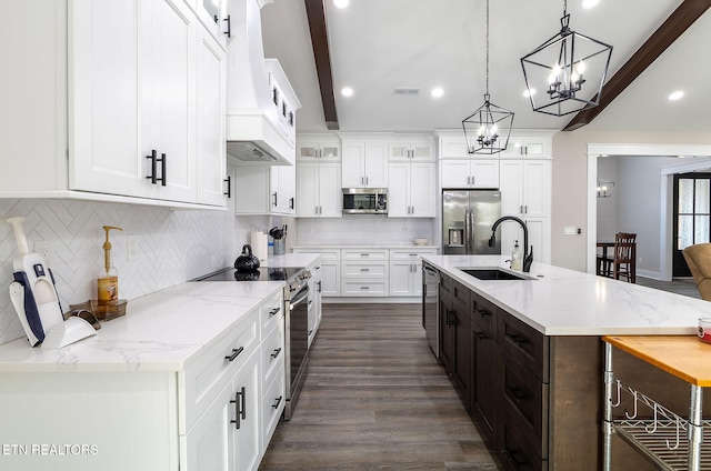 kitchen featuring sink, appliances with stainless steel finishes, beam ceiling, an island with sink, and pendant lighting