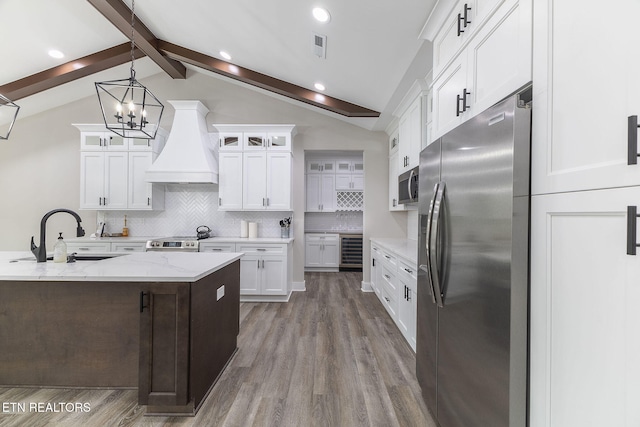 kitchen featuring tasteful backsplash, premium range hood, vaulted ceiling with beams, stainless steel appliances, and decorative light fixtures