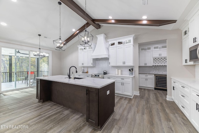 kitchen featuring sink, custom range hood, beverage cooler, a kitchen island with sink, and decorative backsplash