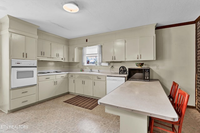 kitchen with light tile patterned flooring, white appliances, sink, and kitchen peninsula