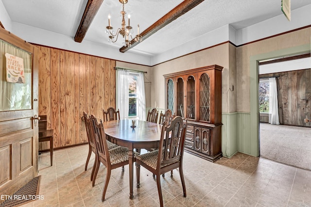 carpeted dining room featuring plenty of natural light, wood walls, beam ceiling, and an inviting chandelier