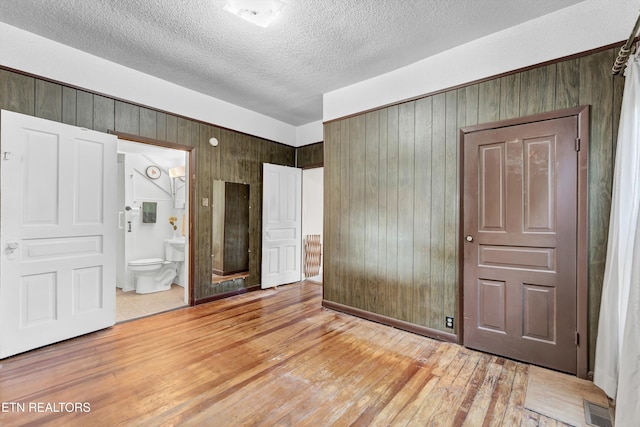 unfurnished bedroom featuring ensuite bathroom, light wood-type flooring, a textured ceiling, and wooden walls