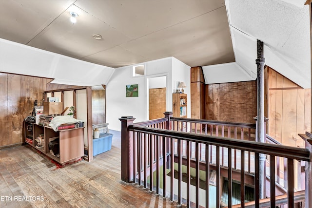 hallway with wood-type flooring, wooden walls, and lofted ceiling