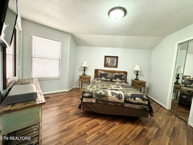 bedroom with dark wood-type flooring, a textured ceiling, lofted ceiling, and a closet